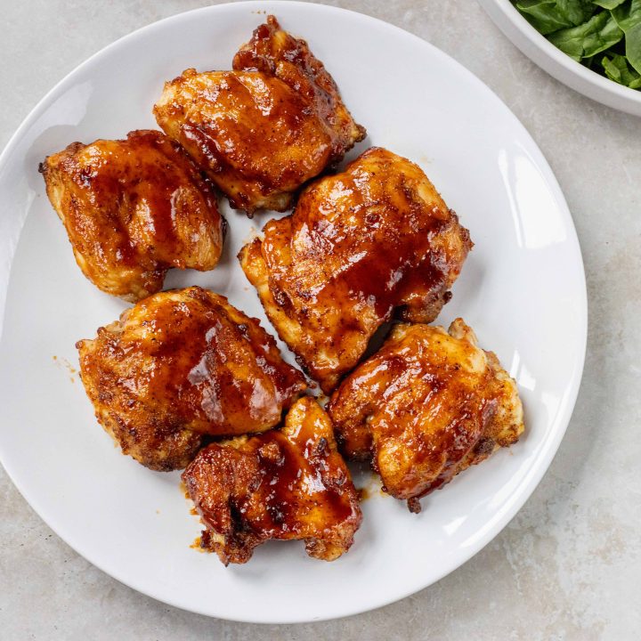 BBQ Chicken Thighs on a plate with salad in the background.