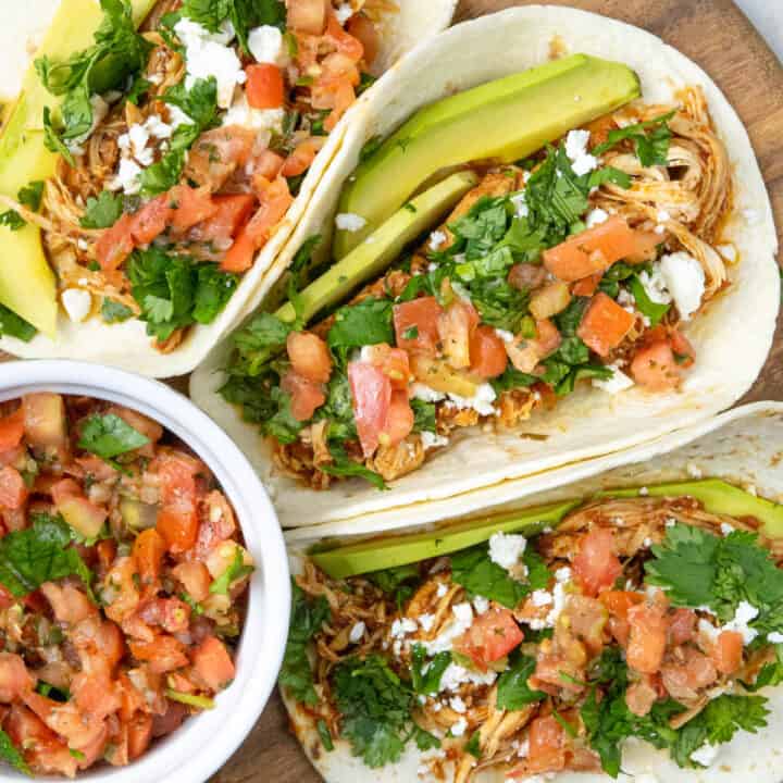 chicken tacos with toppings on a platter with pico de gallo. Slow cooker in the back ground