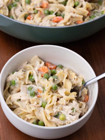 finished bowl of chicken noodle pasta with pan of food in the background