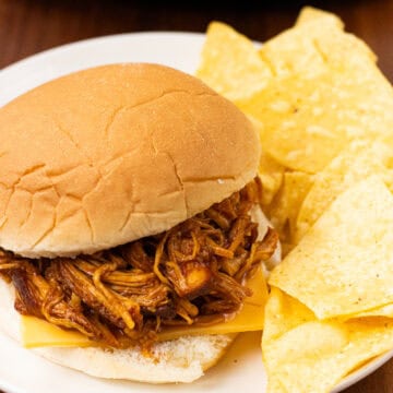 finished Slow Cooker BBQ Chicken in a bun with cheese and chips