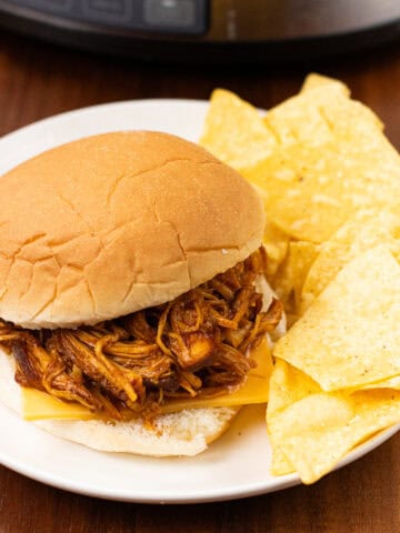 finished Slow Cooker BBQ Chicken in a bun with cheese and chips
