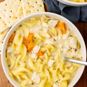 chicken noodle soup in a bowl with crackers on the side